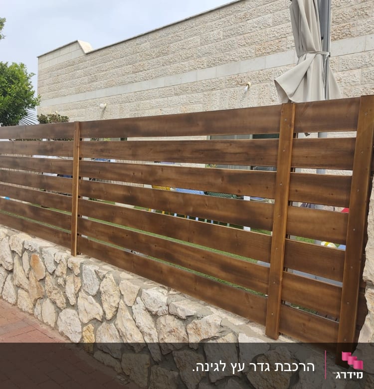 גדר עץ חומה על קיר אבן בגינה